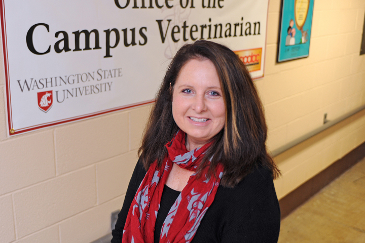 Gay Lynn Clyde, WSU microbiology alumna, standing in front of the Office of the Campus Veterinarian sign.