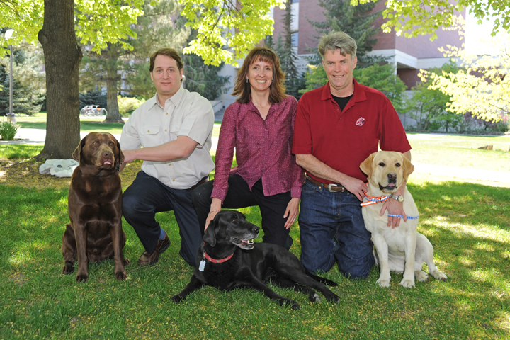 Nicolas Villarino with a chocolate lab, Katrina Mealey with a black lab, Michael Court with a yellow lab.