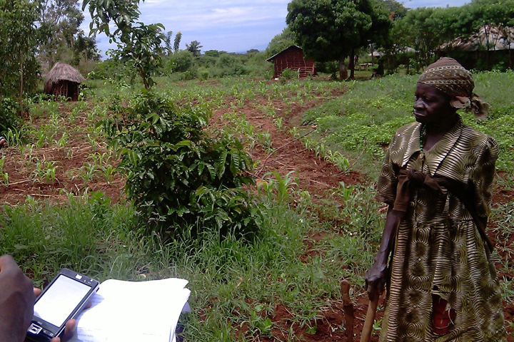 Two Kenyan community volunteers standing in a field conducting the interview with a Kenyan woman.