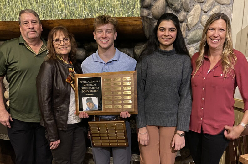 Group standing in from on a fireplace, Peyton is holding the plaque which records each year's recipients.