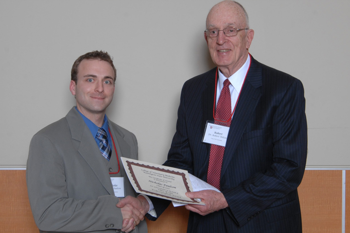 Dr. Willson is holding the certificate and he and Nicholas Paulson are shaking hands.