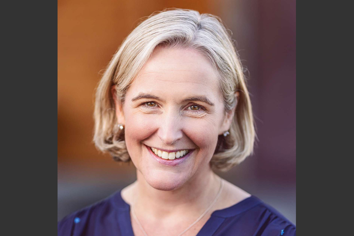 Molly, wearing a navy blue top, the background is blurry, but is orange and blue.