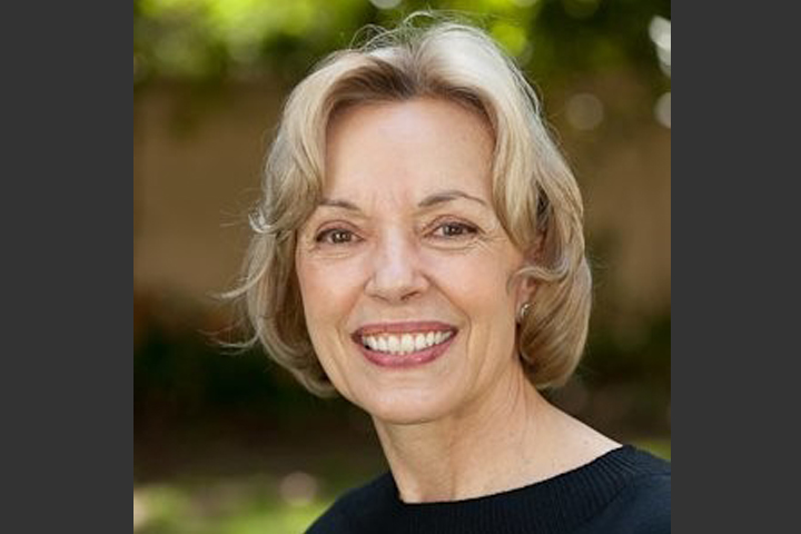 Barb wearing a black top. She's outside with greenery and brick behind her.