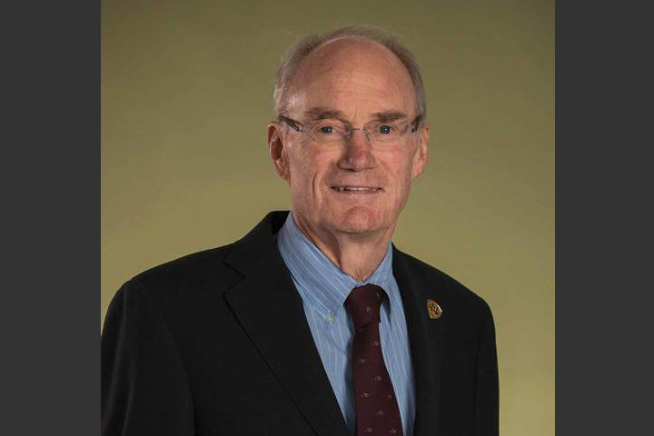 Photo is a photo studio. Joe is wearing a suit and tie, background is tan.