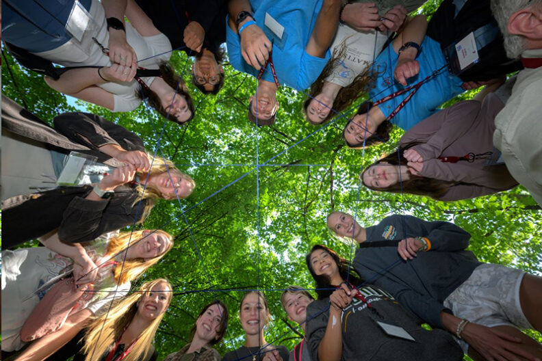 Group activity. Students holding string. Photo from the ground looking up into a dense cover of trees.