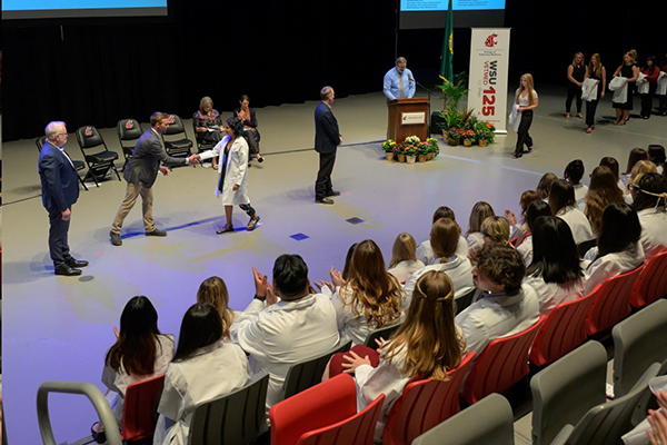 Students receiving their white coats on the stage at Beasley Coliseum.
