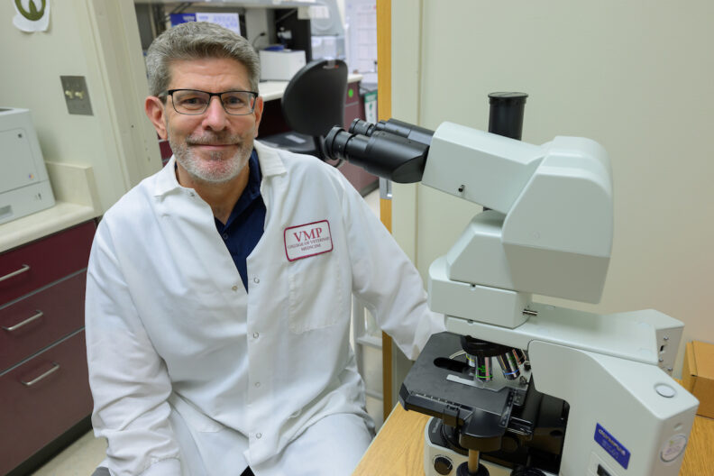 Dr. Troy Bankhead poses next to a microscope in his lab.