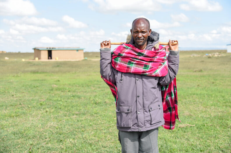Kone wearing a heavy coat and traditional garb with his home in the background.