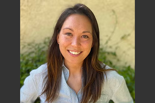 Anna outside with greenery behind her. She is wearing a light blue casual dress shirt.