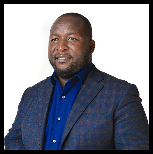 Hillary in the photo studio. He is wearing a royal blue dress shirt with a plaid suit jacket.
