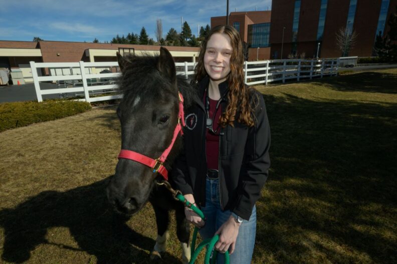 Veterinary student Taylor Veach poses next to a horse.