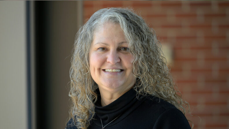 Cindy, outside, with a brick wall at a distance behind her.