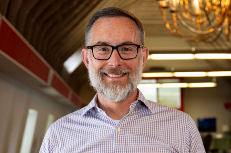 Dr. Oatley in a room with high ceiling. He is wearing a dress shirt and the background is blurry.