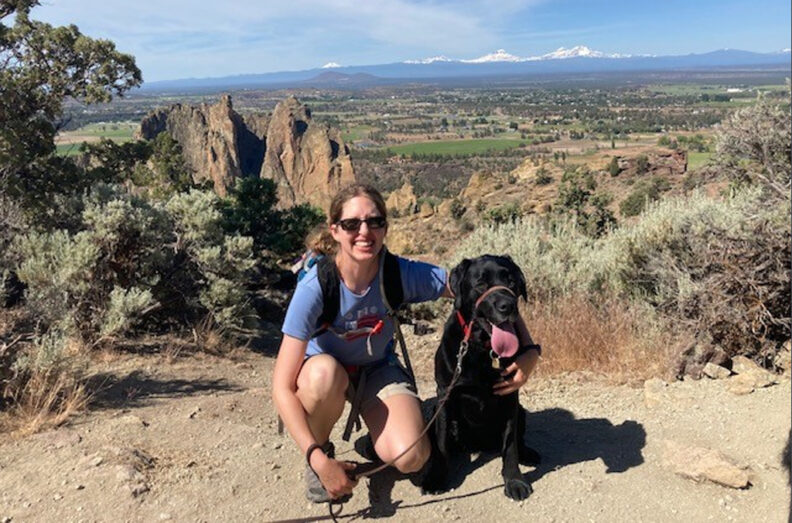 Christina with her dog, a black lab, on a hike in a high desert area.