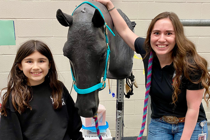 First-year vet student with young girl with the horse head simulator where you can learn how to put a halter on a horse.