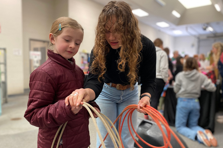 An elementary age student getting instructions on how to hold the rope before she practices roping a stationary calf.
