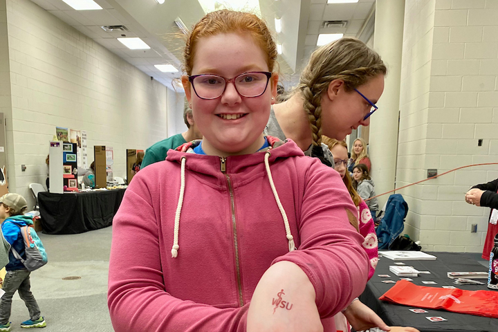 Middle-school age girl showing off the temporary WSU tattoo she just got on her hand.