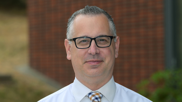 Todd outside the Allen School with a brick building in the distance behind him.