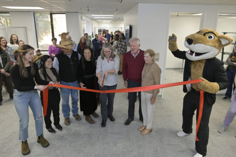 Seven people with Butch. Dean Dori Borjesson is about to cut the ribbon. L-R Two students, Dr. Joseph Bahe and his wife, Alberta Arviso, dean Borjesson in the center, Kandy and Rick Holley, and last but not least, Butch on the far right, holding the ribbon.