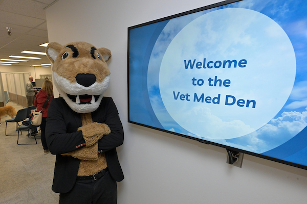 Butch standing next to the digital sign in the Vet Med Den. A "Welcome" slide is displaying.