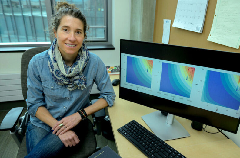 Erin Clancey in her office with her computer monitor displaying graphs from here research.