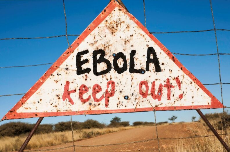 A triangle shaped sign on a hogwire fence warns people of an Ebola virus outbreak in Africa.