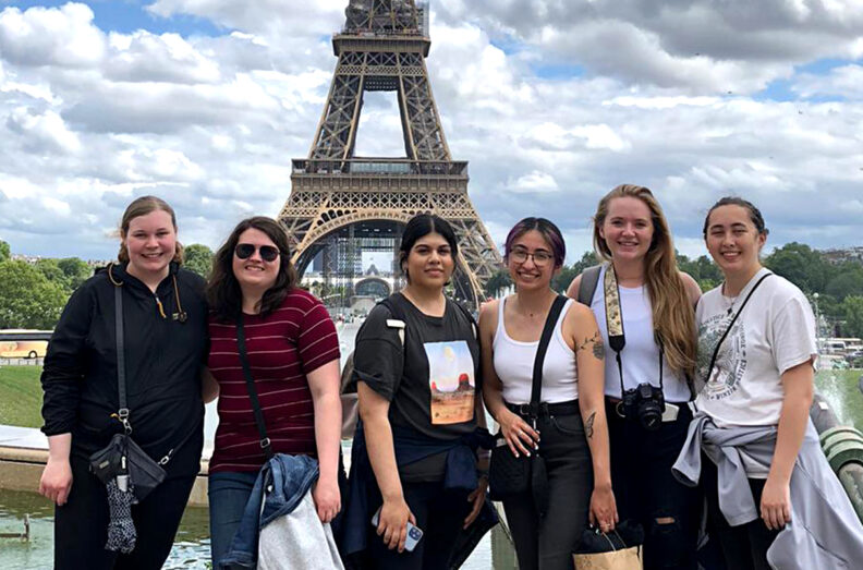 Six students posing with the Eiffel Tower in the distance.
