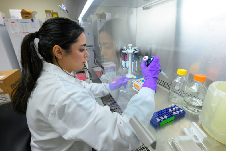 Nafise Noroozi, wearing a white coat and purple protective gloves, works in her lab.