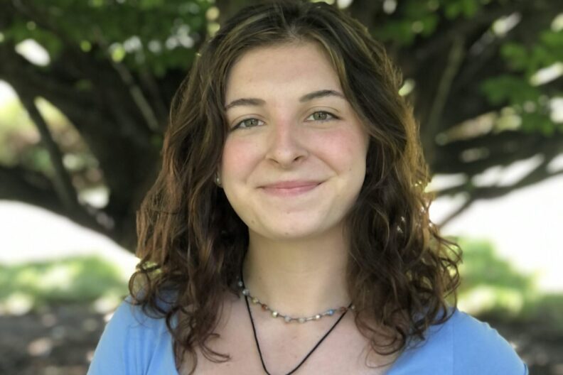 Maddie Muir poses for a photo in front of a tree.