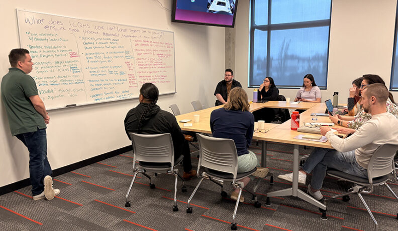 Cole standing a white board full of ideas from a group in the room.