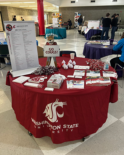 Round merch table set up in large room with many other tables. 