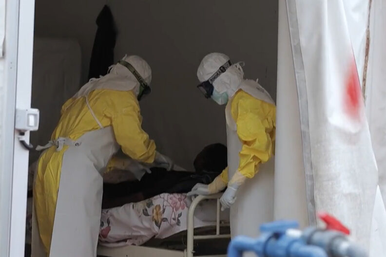 Eboal patient in a tent with two people, in full PPE, attending.