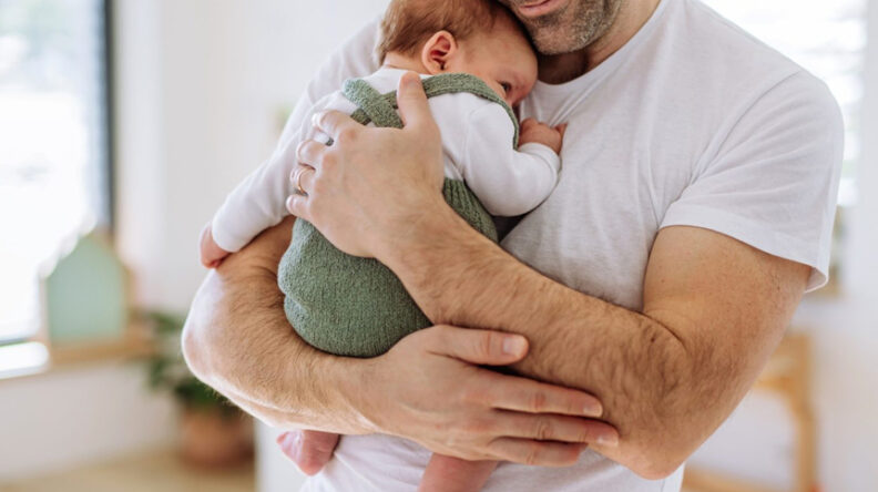 Father in white t-shirt, holding infant against his chest.