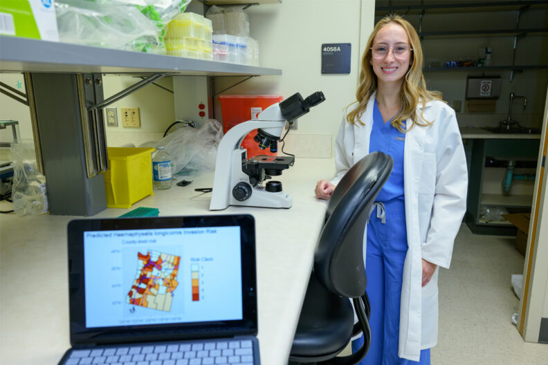 Caroline standing in a lab at a counter with a microscope.