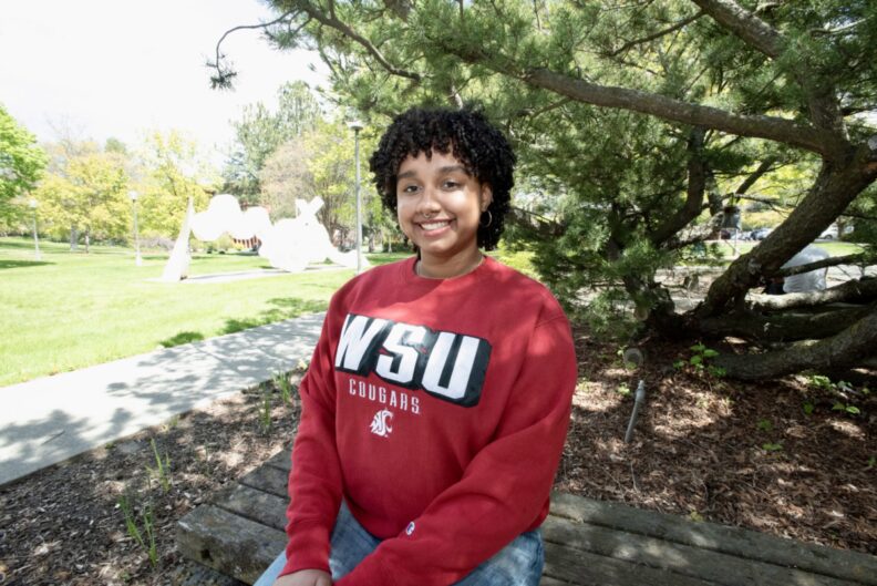 Ari Wilson, wearing a WSU sweatshirt, poses in front of a tree.