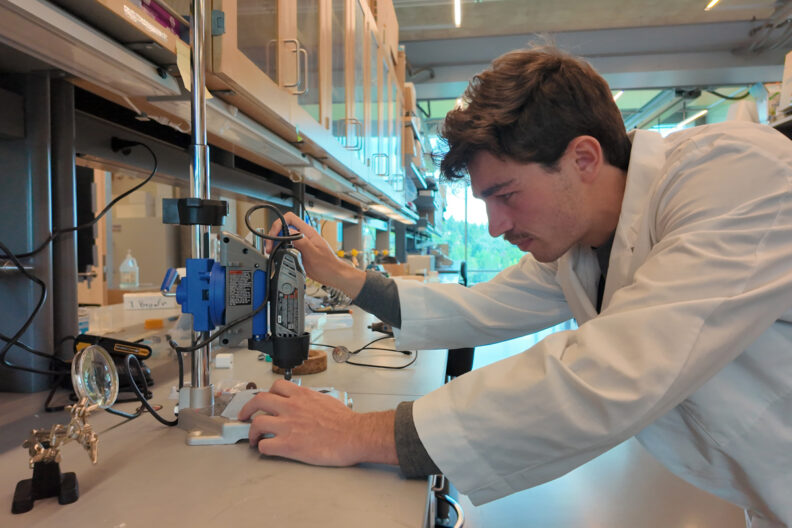 Ari in a lab with multiple tools on the workspace he is bent over at.