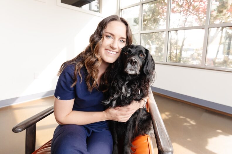Jess posing with her dog as both are seated in a chair.