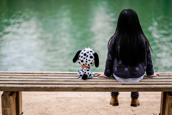 Young girl on a bench with a stuffed dog next to her.