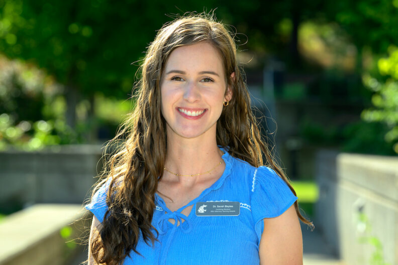 Dr. Sarah Bayles, wearing blue scrubs, poses for a photo outside of the VTH.