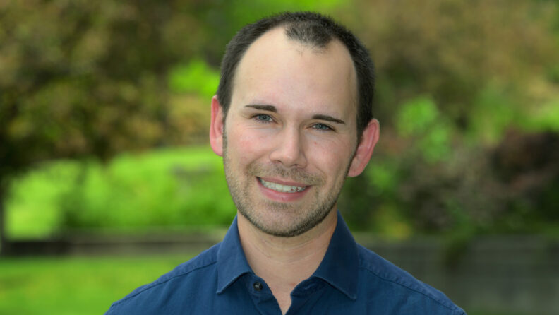 Dr. Miller outside on a sunny day. He's wearing a dark blue button up shirt.