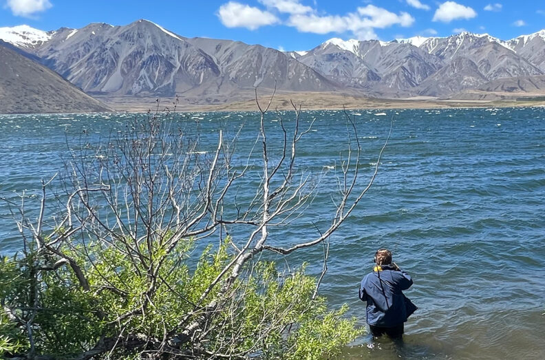A Maori tribal youth fishes in the foreground, at Lake Heron.