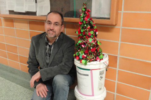 Man kneeling in a hallway next to a small Christmas tree.