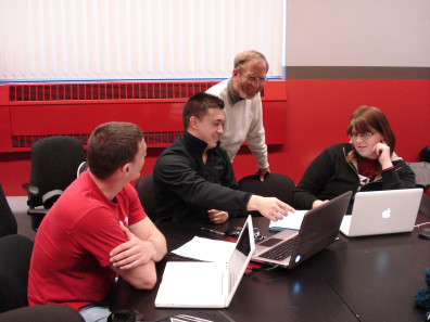 Student pointing to laptop while professor and two other students observe.