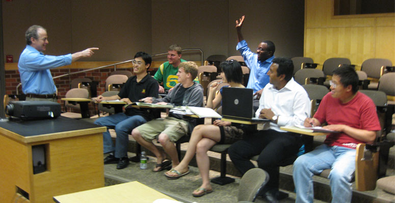 Lecture hall with a professor pointing at a student who is raising their hand.