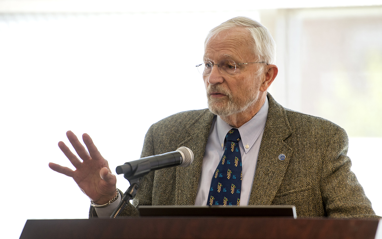 David Ensor gestures with his hand from behind a speaker podium.