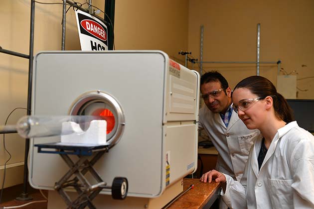 Two people in white lab coats looking in to a machine.