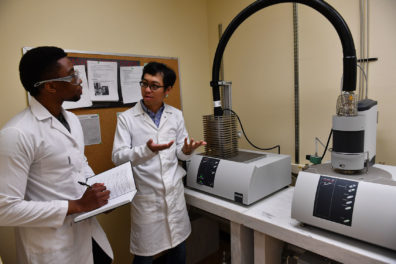 Student writing in notebook while professor speaks and gestures with his hands.