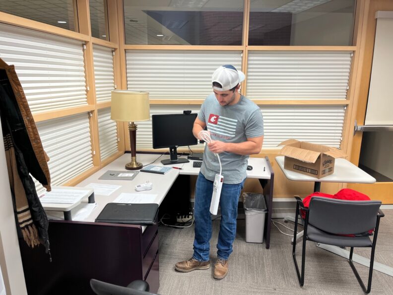Jacob-Roibal-installing-a-smart-power-strip-in-a-WSU-office.