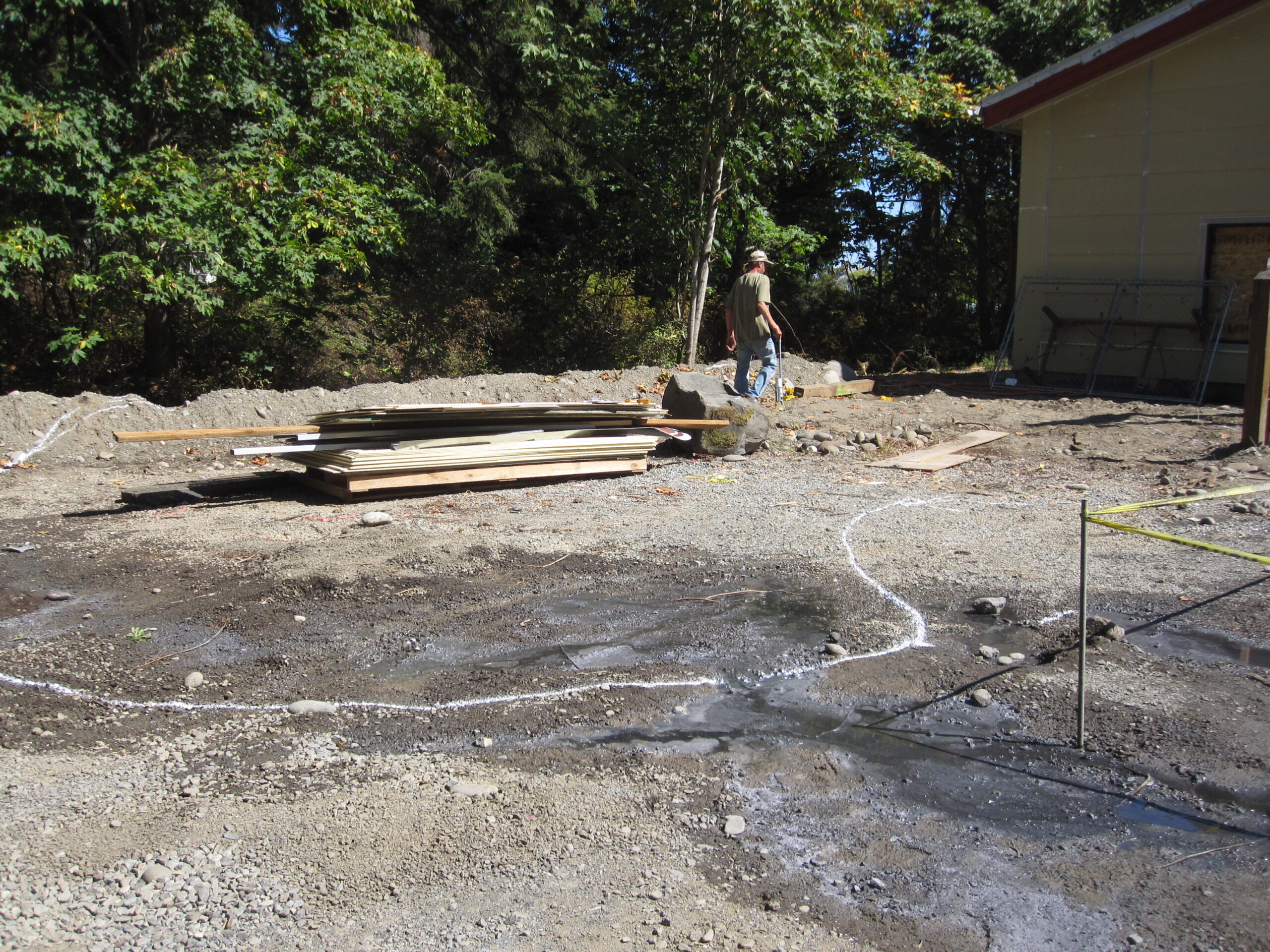 Construction area, outline of rain garden on ground, man measuring