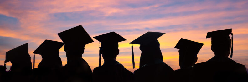 Silhouettes of students with graduate caps in a row on sunset background.